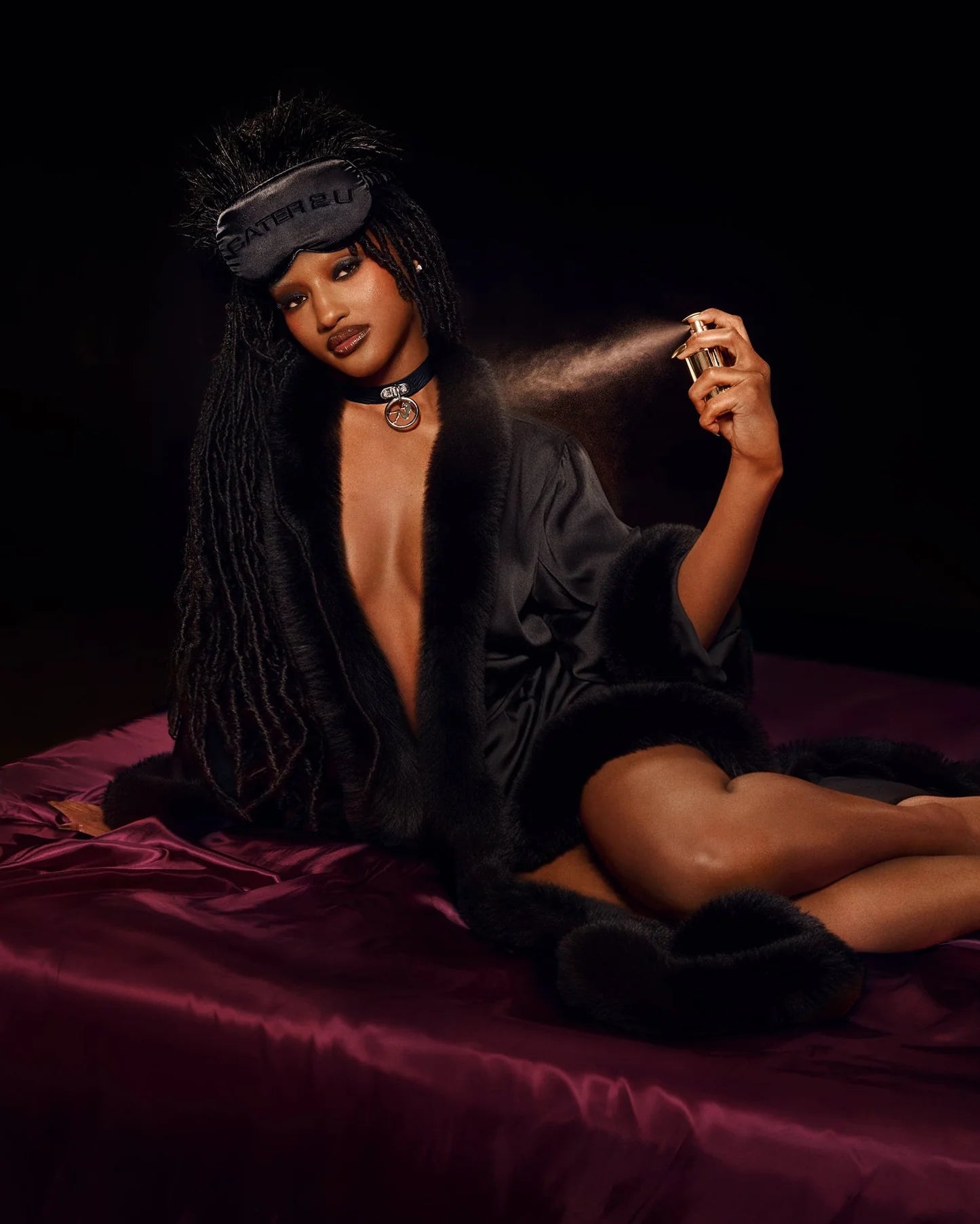 Model wearing black robe with fur trim spraying fragrance with accessories in styled setting