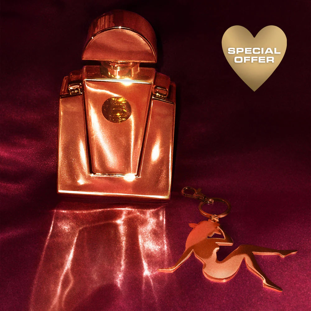 Gold Cé Lumière perfume with Lady Bey charm keychain on red satin background with special offer badge